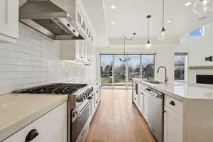 Kitchen with a sink, stainless steel appliances, decorative backsplash, and wall chimney range hood