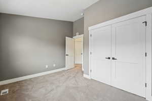 Unfurnished bedroom featuring a closet, visible vents, light colored carpet, and baseboards