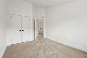 Unfurnished bedroom featuring a closet, baseboards, and light colored carpet