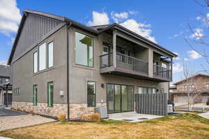 Rear view of house featuring stucco siding, a lawn, board and batten siding, a balcony, and central AC unit