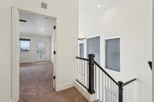 Hall with visible vents, an upstairs landing, baseboards, and carpet flooring