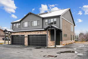 View of front facade with stone siding, driveway, a garage, and board and batten siding