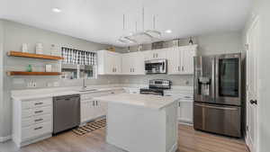 Kitchen featuring stainless steel appliances, light wood-style flooring, white cabinetry, and a sink