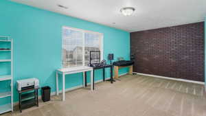 Carpeted office space featuring visible vents, brick wall, a textured ceiling, and baseboards