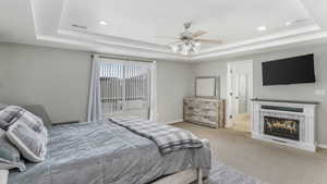 Carpeted bedroom with visible vents, a raised ceiling, baseboards, and a glass covered fireplace