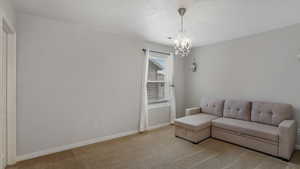 Carpeted living area with visible vents, baseboards, and an inviting chandelier