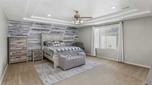 Carpeted bedroom featuring visible vents, baseboards, an accent wall, and a tray ceiling