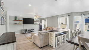 Living room with light wood-style flooring, a ceiling fan, a textured ceiling, recessed lighting, and baseboards