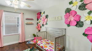 Bedroom featuring multiple windows, a crib, baseboards, and wood finished floors