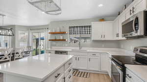 Kitchen with a textured ceiling, light countertops, a sink, stainless steel appliances, and light wood finished floors