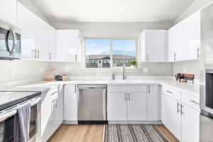 Kitchen featuring a sink, white cabinetry, appliances with stainless steel finishes, and light wood finished floors