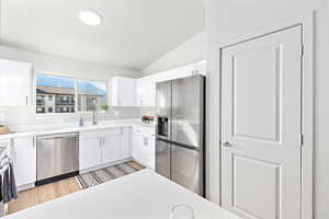 Kitchen featuring light countertops, vaulted ceiling, stainless steel appliances, white cabinetry, and a sink