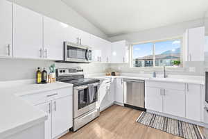 Kitchen featuring a sink, stainless steel appliances, vaulted ceiling, white cabinetry, and light wood-type flooring