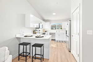 Kitchen featuring stainless steel appliances, light wood-style floors, a peninsula, a breakfast bar area, and white cabinets