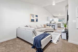 Living room featuring vaulted ceiling, recessed lighting, baseboards, and light carpet