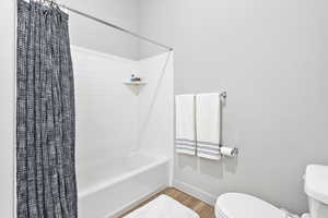 Full bathroom featuring toilet, shower / tub combo with curtain, baseboards, and wood finished floors