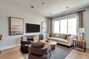 Living room with visible vents, baseboards, light wood finished floors, and a textured ceiling