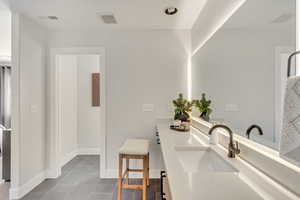 Full bath with double vanity, visible vents, baseboards, and a sink