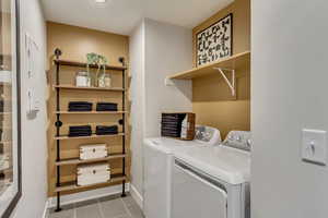 Clothes washing area with washer and clothes dryer, laundry area, tile patterned flooring, and baseboards