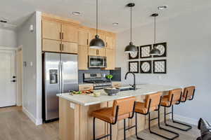 Kitchen featuring light brown cabinetry, tasteful backsplash, light wood-style floors, appliances with stainless steel finishes, and a peninsula
