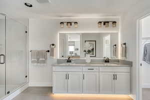 Bathroom with tile patterned flooring, double vanity, a stall shower, and a sink