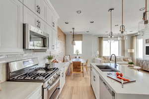 Kitchen with a sink, open floor plan, stainless steel appliances, light wood finished floors, and decorative backsplash