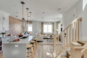 Kitchen with a breakfast bar area, light wood finished floors, a kitchen island with sink, a sink, and open floor plan