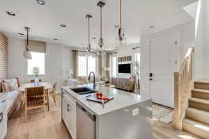 Kitchen featuring light wood finished floors, open floor plan, dishwasher, and a sink