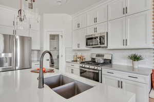 Kitchen featuring a sink, backsplash, white cabinetry, appliances with stainless steel finishes, and light countertops