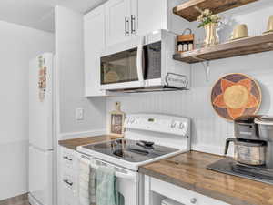 Kitchen with white appliances, white cabinets, open shelves, and butcher block countertops