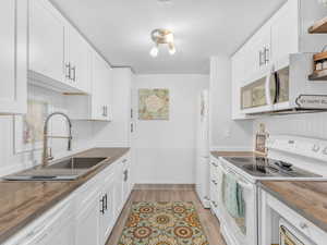 Kitchen featuring butcher block countertops, light wood-style flooring, white cabinets, white appliances, and a sink