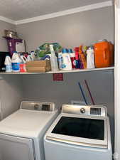 Clothes washing area with washer and clothes dryer, a textured ceiling, and crown molding