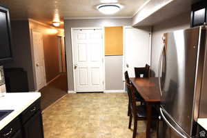 Kitchen with crown molding, light countertops, freestanding refrigerator, a textured ceiling, and dark cabinets