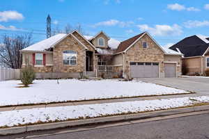 View of front of property with stone siding, driveway, an attached garage, and fence