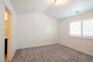 Carpeted spare room with visible vents, baseboards, and vaulted ceiling