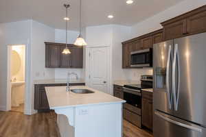 Kitchen featuring an island with sink, a sink, dark brown cabinetry, light wood-style floors, and appliances with stainless steel finishes