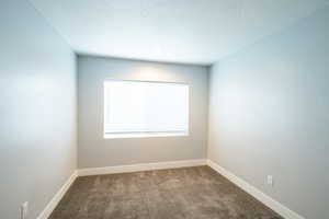 Unfurnished room featuring dark colored carpet, baseboards, and a textured ceiling
