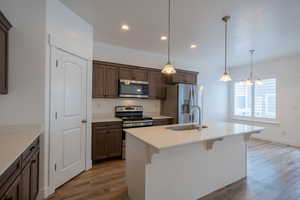 Kitchen featuring a center island with sink, light wood-type flooring, recessed lighting, stainless steel appliances, and a sink
