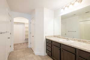 Bathroom with vanity, baseboards, visible vents, a walk in closet, and tile patterned floors