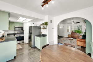 Kitchen featuring green cabinetry, arched walkways, a sink, appliances with stainless steel finishes, and dark countertops