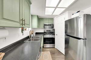 Kitchen featuring a sink, dark countertops, wood finished floors, stainless steel appliances, and green cabinetry