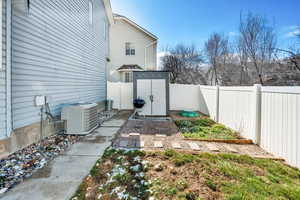View of yard with a shed, central AC, a fenced backyard, an outdoor structure, and a garden