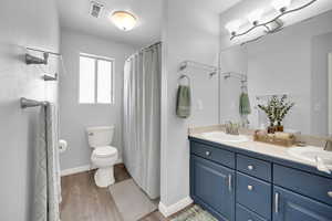 Bathroom with double vanity, toilet, wood finished floors, and a sink