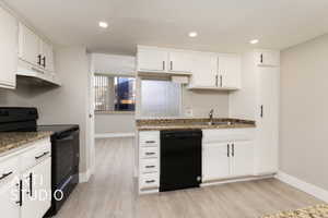 Kitchen with under cabinet range hood, light wood-style floors, white cabinets, black appliances, and a sink