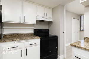 Kitchen featuring under cabinet range hood, white cabinets, stone countertops, and black range with electric stovetop