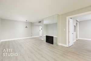 Unfurnished living room with a fireplace, light wood-style floors, visible vents, and baseboards