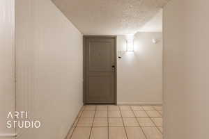 Hallway featuring light tile patterned floors, a textured ceiling, and baseboards