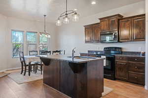 Kitchen with a sink, stainless steel microwave, black / electric stove, and light wood-style floors