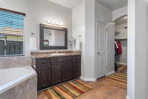 Full bath featuring vanity, wood finished floors, baseboards, a relaxing tiled tub, and a walk in closet