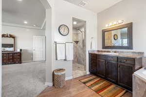 Bathroom with visible vents, walk in shower, wood finished floors, and vanity